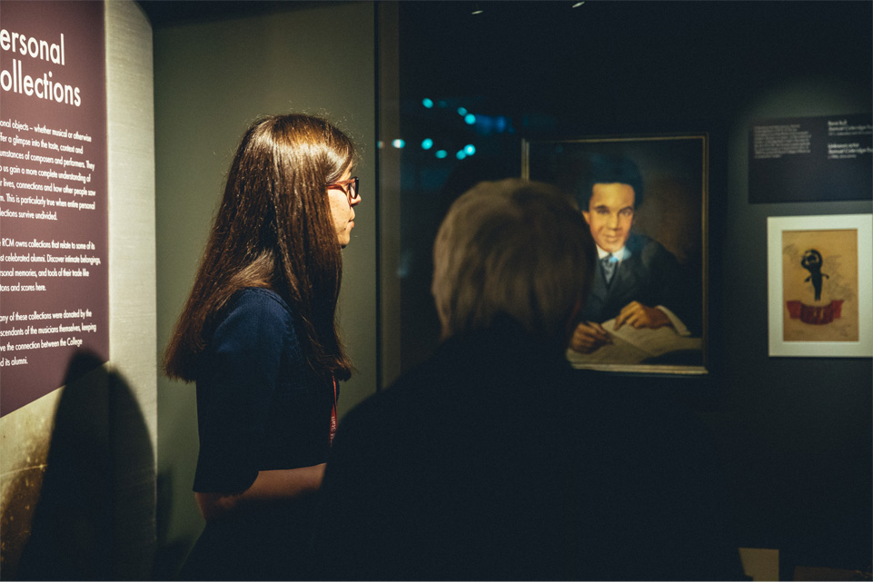 A women looking at a painting at the RCM Museum, with another visitor with short grey hair looking beside them.